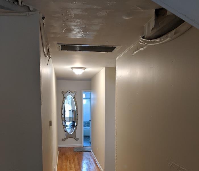 Hallway with wood floors and water damage to the ceiling and walls