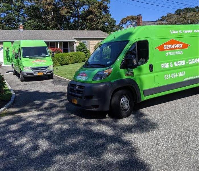Two Green SERVPRO trucks in front of a house.